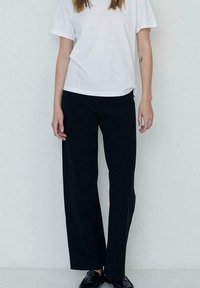 Pantalones anchos y negros hechos de una tela suave, combinados con una camiseta blanca de manga corta de corte holgado. Diseño simple, con detalles mínimos.