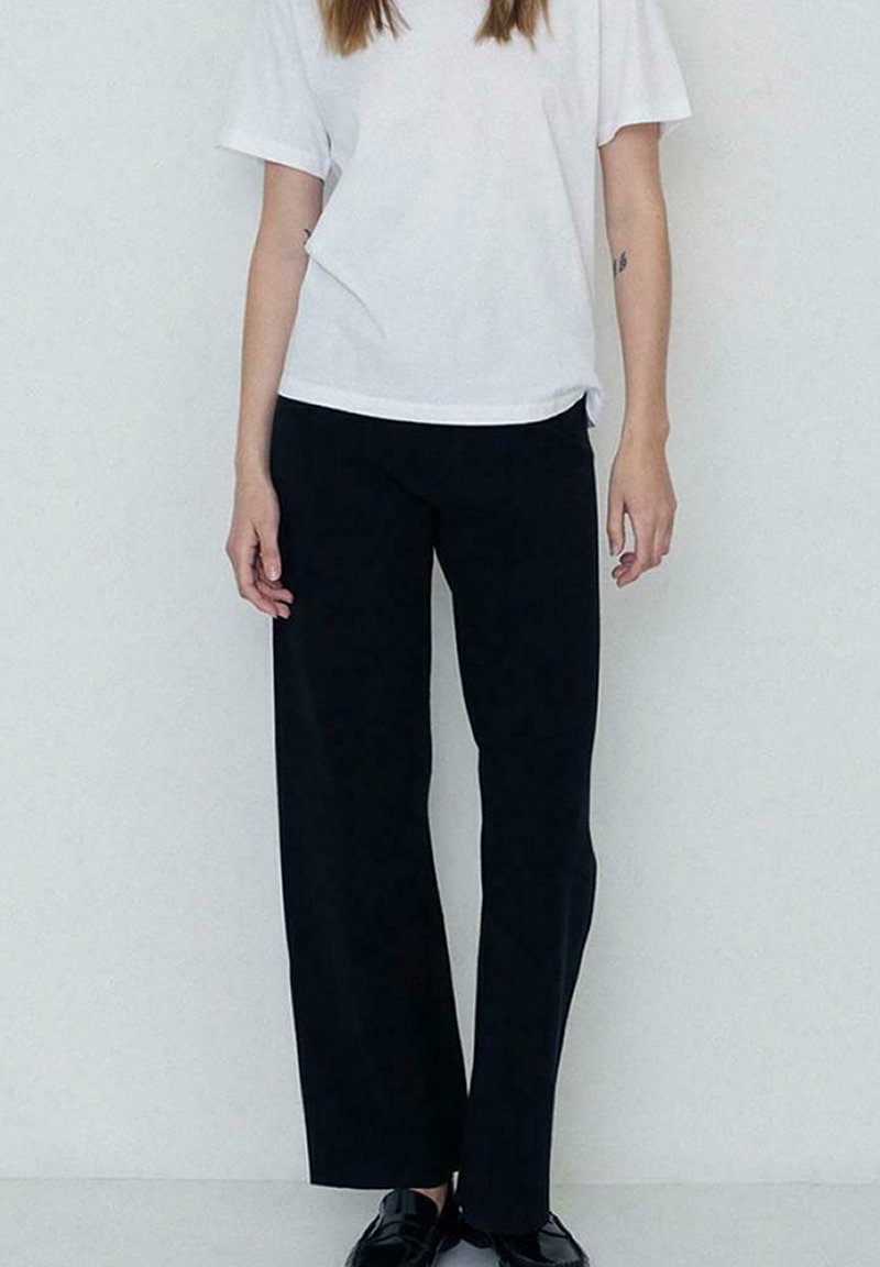 Pantalones anchos y negros hechos de una tela suave, combinados con una camiseta blanca de manga corta de corte holgado. Diseño simple, con detalles mínimos.