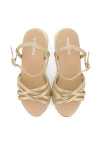 Sandalias de tacón alto beige con un diseño entrelazado, que presentan tiras brillantes, un hebilla en el tobillo y una suela suave de color claro.