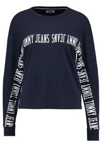 Navy long-sleeve sweatshirt with white "TOMMY JEANS" text along the sleeves. Made of soft fabric; rounded neckline, relaxed fit.