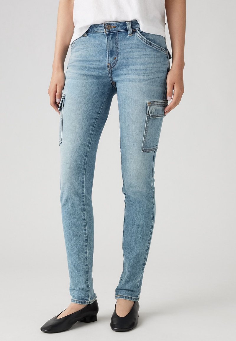 Vaqueros cargo de mezclilla ajustados en un azul claro con dos bolsillos laterales, un diseño clásico de cinco bolsillos y un ligero desgaste, combinados con zapatos negros planos.