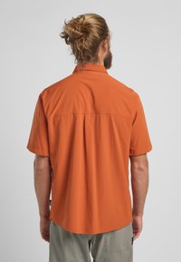 Korte mouwen shirt in oranje, met een klassieke kraag, rechte zoom en zijsplitten. Gemaakt van lichtgewicht stof, met een achterpand detail.