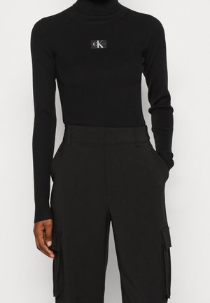 Black ribbed turtleneck with long sleeves featuring a logo patch. Paired with black cargo pants having side pockets and a smooth finish.