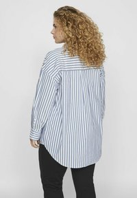 Camisa de botones a rayas en azul claro y blanco, con dobladillo curvado, mangas largas y detalle de pliegue en la parte posterior, hecha de tela ligera.