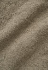 Tissu en lin beige avec une texture légèrement froissée et des fibres tissées visibles, créant une apparence douce et naturelle.