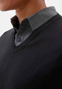 Schwarzer V-Ausschnitt-Pullover mit einem strukturierten, dunkelgrauen Kragen, der mit einem Knopfdetail versehen ist. Weicher Stoff, enganliegendes Design, das den Ausschnitt betont.