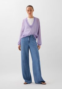 Lila V-hals trui met losse mouwen, gecombineerd met high-waisted, wijde blauwe jeans. Glad materiaal met een relaxte pasvorm en eenvoudig ontwerp.