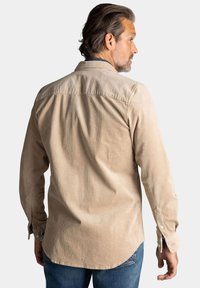 Beige corduroy overhemd met een button-down kraag, zichtbare textuur en lange mouwen. Voorzien van een yoke-detail en verstelbare manchetten.