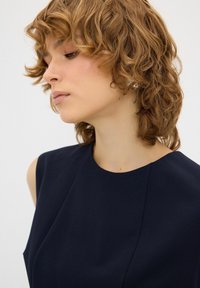 Vestito senza maniche blu navy con scollatura rotonda, texture liscia e dettagli delle cuciture sottili. Capelli corti e mossi visibili di profilo.