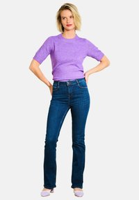 Svetro s kratkimi rokavi v lavandulasti barvi, v kombinaciji s temno modrimi hlačami z visokim pasom in širokimi nogami. Model nosi svetlo vijolične petke. Gladka pletenina.