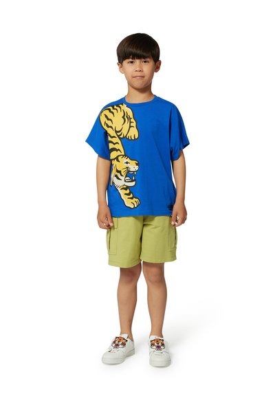 T-shirt en coton bleu avec un graphique amusant de tigre, associé à un short cargo vert clair et des baskets blanches avec un design de tigre.