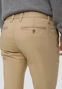 Chinos kaki en tissu mélangé de coton, avec une texture lisse, une coupe fuselée, deux poches arrière et une fermeture à un bouton.