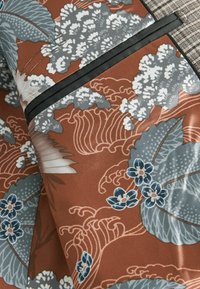 Stoff mit braunem Hintergrund, der florale Muster in Grau und Blau zeigt, akzentuiert mit schwarzem Rand und komplexen Texturen.