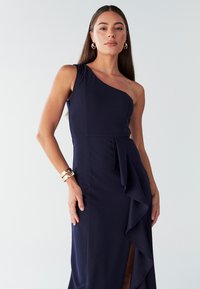 Tumesinine ühe õlaga kleit, millel on keha järgnev ülaosa, asümmeetriline disain ja eesmine volditud detail. Sile tekstuur ja külje lõhike lisavad elegantsi.