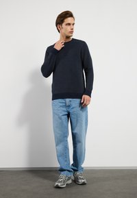 Suéter de punto azul marino con un patrón texturizado, combinado con jeans azul claro y zapatillas grises, con un ajuste relajado.
