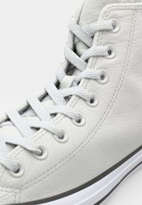 Høytop sneakers laget av strukturert hvitt lær. Har grå snøringer, hvite lisser og en kontrasterende grå gummisåle.