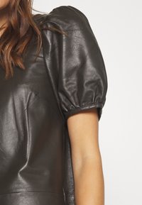 Top in pelle nera con maniche corte a sbuffo, caratterizzato da una texture liscia e una linea arrotondata sulle spalle. Taglio semplice, senza elementi hardware o motivi visibili.