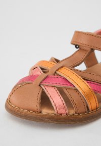 Bruine leren sandaal met kruislings banden in roze, oranje en tan. Heeft een open teenontwerp en gestikte accenten op de zool.