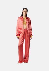 Set di abbigliamento casual in satin corallo composto da una camicia a maniche lunghe con bottoni e tasche e pantaloni larghi abbinati, completati da un top giallo.