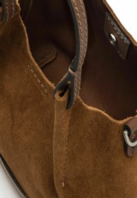 Borsa a mano in suede marrone con manici e cuciture in pelle marrone scuro, dotata di un interno liscio e un accento in metallo argentato.
