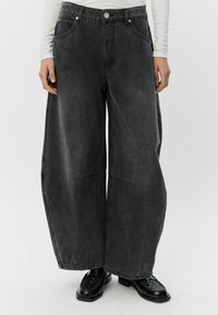 Široke, visoko pasové črne kavbojke z sprednjimi žepi in zbledelim zaključkom, s podvojenimi šivi in srebrnimi gumbki.