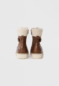 Bottines en cuir marron avec un bord en fourrure beige, fermeture éclair et une semelle légère crème. Présente une boucle décorative sur le côté.