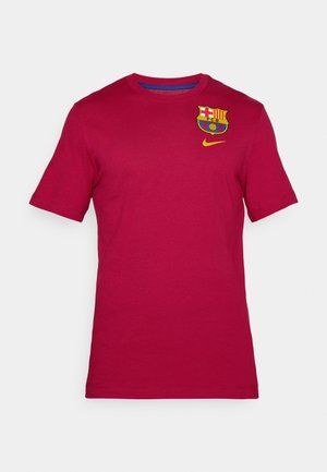 Crvena pamučna majica s okruglim izrezom. Na lijevoj strani prsa ima logo Barcelone, a ispod njega žuti Nike simbol. Kratki rukavi.