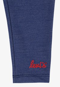 Sötétkék farmer anyag, finom textúrával; vörös "Levi's" logó hímzett a szegély közelében, egyenes szabással.