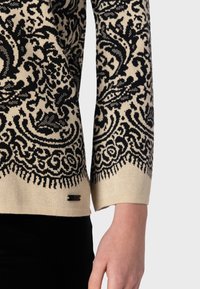 Pull noir et crème avec des motifs floraux complexes, en tissu tricot doux, manches trois-quarts et un bord inférieur décoratif.