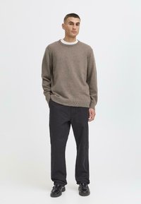 Light brown wool sweater with a crew neckline, paired with dark, loose-fit trousers and black shoes. Simple design, no patterns.