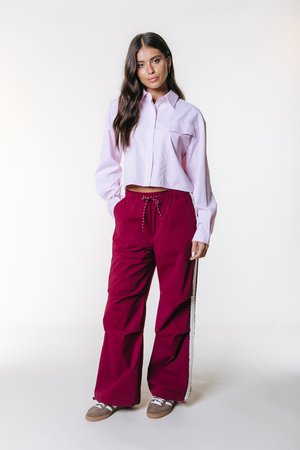 Világos rózsaszín, rövidített, hosszú ujjú, gombos ing mellzsebbel, bordó széles szárú nadrággal, oldalsó csíkkal és húzózsinórral.