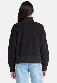 Svart croppad sweatshirt med hög krage, sänkta axlar och ribbade ärmslut. Har en mjuk textur och avslappnad passform, perfekt ihop med ljus denim.