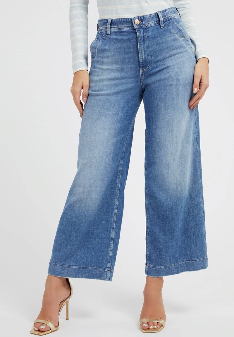 Vaaleansiniset leveälahkeiset farkut denim-kankaasta, joissa on korkea vyötärö, nappikiinnitys sekä hillitty kuluminen ja voimakkaat tikkaukset.