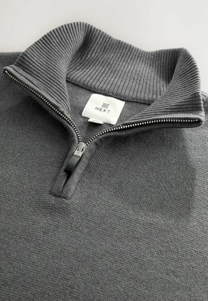 Sivi zipper dukserica s rebrastim ovratnikom, teksturiranom tkaninom i malom oznakom logotipa. Ima srebrni patentni zatvarač s crnom kvačicom.