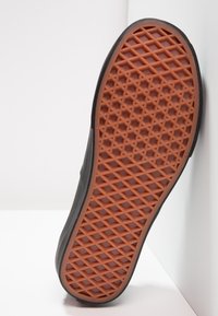 Suela de zapato negra con un patrón geométrico, con una banda de rodadura de goma naranja que proporciona agarre y tracción. El borde es ligeramente redondeado.