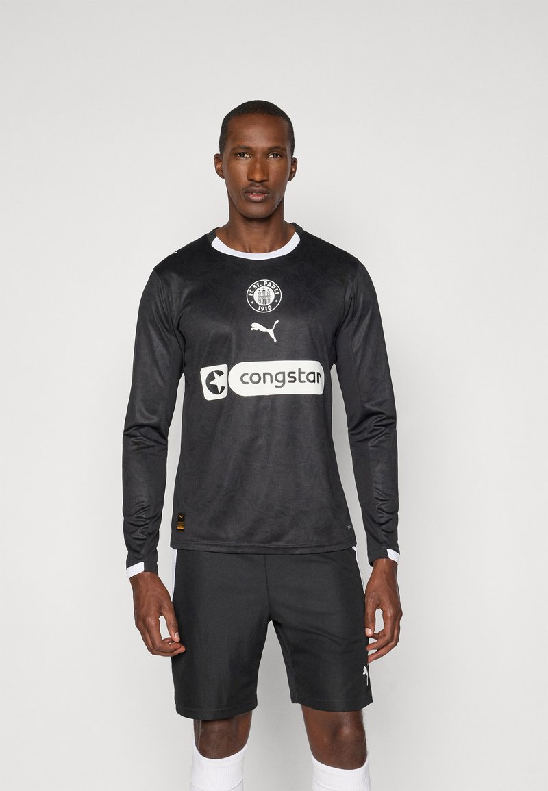 Czarna koszulka piłkarska z długim rękawem i białymi akcentami, z logo FC St. Pauli, logo Pumy oraz logo sponsora na klatce piersiowej. Noszona z czarnymi szortami.