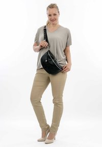 Borsa a tracolla nera in pelle con hardware argentato, texture liscia e forma curva, indossata su una maglia grigia chiara e pantaloni beige.