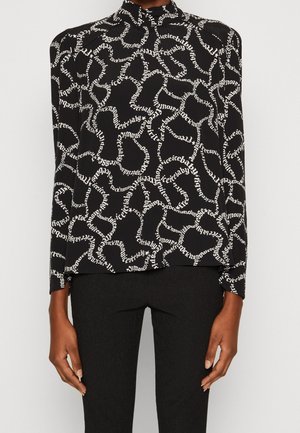 Top nero a maniche lunghe con collo alto, caratterizzato da un motivo di testo bianco a spirale, abbinato a pantaloni neri texturizzati.