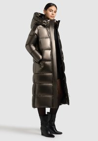 Metallischer Pufferparka mit Kapuze, der rechteckige gesteppten Abschnitte aufweist. Der Mantel ist knielang und verfügt über einen Reißverschluss sowie Seitentaschen. Schwarze strukturierte Stiefel.