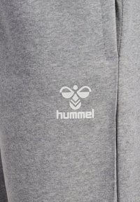 Graue Sweatpants aus weichem Stoff mit einem weißen "hummel"-Logo, das ein Bienen- und Blattdesign auf dem linken Oberschenkel zeigt.
