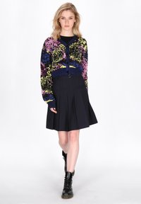 Cardigan corto multicolore con base blu navy e motivo testurizzato. Abbinato a una gonna nera plissettata e stivali neri stringati.