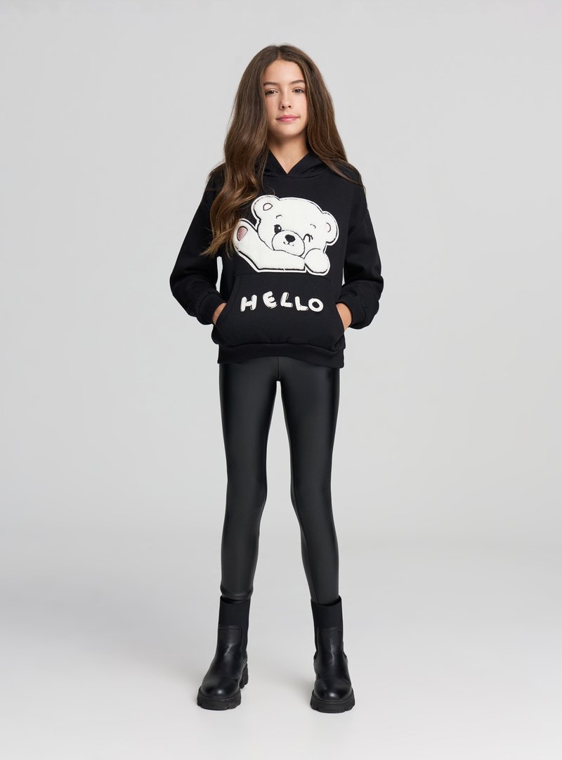 Czarna bluza z kapturem z białą grafiką niedźwiedzia i napisem "HELLO", połączona z czarnymi błyszczącymi legginsami i czarnymi botkami za kostkę.