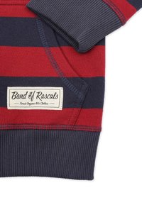 Punainen ja laivastonsininen raidallinen collegepaita, jossa on ribbikujat hihansuissa ja helmassa. Sisältää tikatun taskun ja etiketin, jossa on "Band of Rascals" logo.