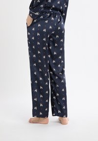 Pantalones de pijama azul marino con acabado de satén, con un estampado repetido de figuras juguetonas y puntos naranjas, cintura elástica, ajuste holgado y bolsillos laterales.