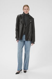 Black leather biker jacket with asymmetric zipper, wide lapels, and two front pockets, paired with light blue straight-leg jeans and black heels.