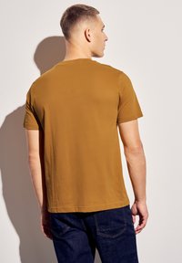 Hnědé tričko s krátkým rukávem a hladkou texturou, s kulatým výstřihem a rovného střihu, kombinované s tmavě modrými džínami.