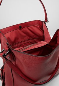 Sac à main en cuir rouge avec une finition texturée, doté d'une poche zippée et d'une fermeture à pression. Intérieur doublé en tissu assorti.