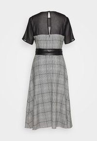 Robe à carreaux noir et blanc avec des manches courtes transparentes noires, une ceinture noire à la taille et un détail du dos en forme de trou de serrure. Design de jupe évasée.
