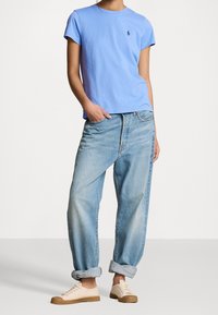 Světle modré tričko s krátkým rukávem a malým logem, doplněné světlými volnými džíny a světle zbarvenými teniskami.