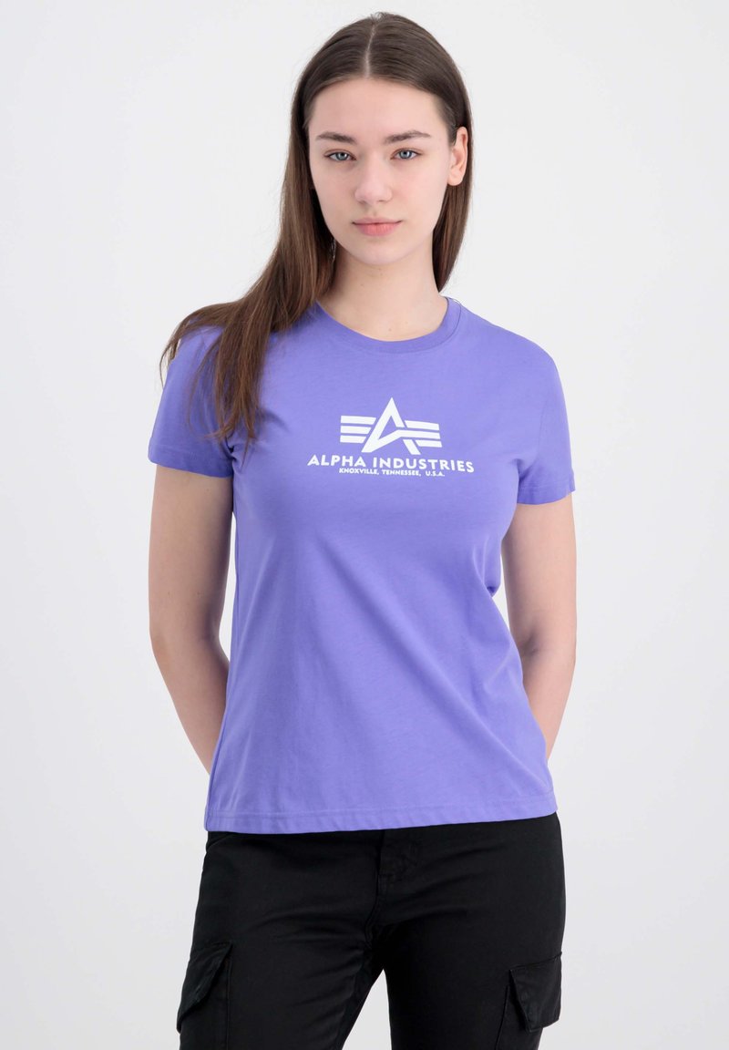 Lilla bomulds t-shirt med korte ærmer og rund halsudskæring. Har en hvid logo-tekst "ALPHA INDUSTRIES" på fronten.